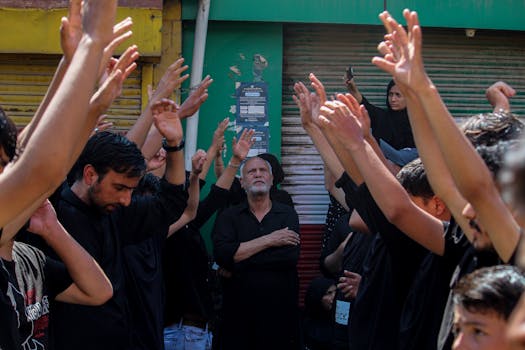 Participants in an Ashura procession in Srinagar raise their hands in a religious gathering outdoors.
